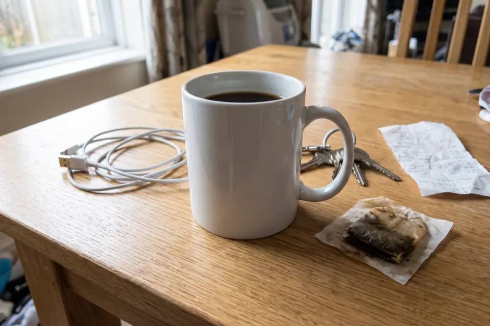 White coffee mug on a wooden table next to a cable, keys, a receipt and a used tea bag
