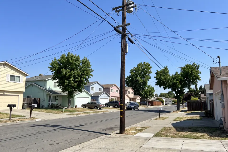 Suburban street with a wooden utility pole and many power lines across the sky